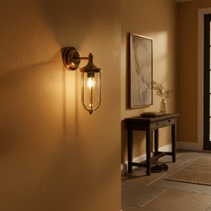 Antique brass outdoor wall lamp with clear glass, illuminating a warm-toned wall in a cozy entryway.