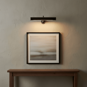 Matt black wall lamp illuminating a framed artwork above a wooden console table.