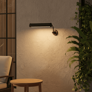 Matt black wall lamp illuminating a textured wall, beside a cozy chair and wooden table.