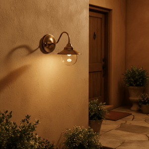 Antique brass outdoor wall lamp with clear glass diffuser, illuminating a warm entrance area.