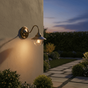 Antique brass outdoor wall lamp with clear glass diffuser, casting warm light on a garden path.