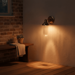 Fabio Hanging Wall Lamp in antique brass illuminating a rustic outdoor setting with a wooden bench and potted plant.