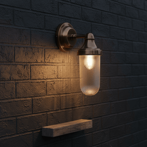 Fabio Hanging Wall Lamp in antique brass mounted on a textured dark brick wall, illuminating a wooden shelf below.
