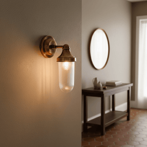 Fabio Hanging Wall Lamp in antique brass with clear glass diffuser, illuminating a stylish indoor setting.