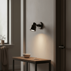 Indigo Swirl Wall Lamp in matt black mounted on a wall, illuminating a wooden table with a bowl and keys.