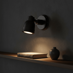 Indigo Swirl Wall Lamp in matte black illuminating a book on a shelf, showcasing its rotatable shade.