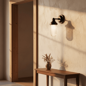 Fabio Hanging Lamp in Matt Black mounted on a textured wall, casting a soft shadow, with a wooden table and vase nearby.