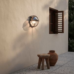 Nautical wall light mounted on a textured wall, illuminating a rustic stool and terracotta pot.
