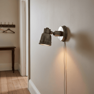 Antique silver wall lamp with adjustable shade mounted on a light-colored wall, illuminating the space.