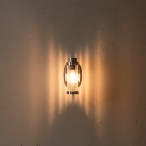 Antique silver wall lamp with acrylic tube design casting warm light on textured wall.