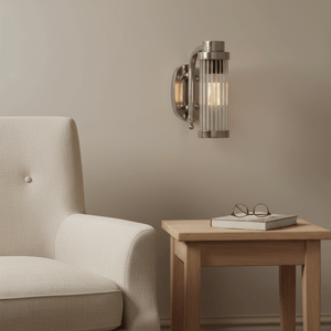 Antique silver wall lamp mounted beside a cozy armchair and wooden side table with a book and glasses.