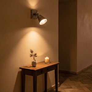 Antique silver wall lamp illuminating a wooden table with a vase and candle.