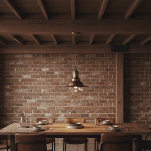 Wellington Hanging Lamp in antique brass above a rustic dining table with wooden chairs and a brick wall backdrop.