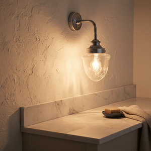 Antique silver wall lamp with cut glass design illuminating a marble countertop, featuring a plate with soap.