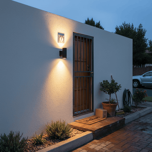 Black outdoor wall light illuminating entrance with plants and a welcome mat.