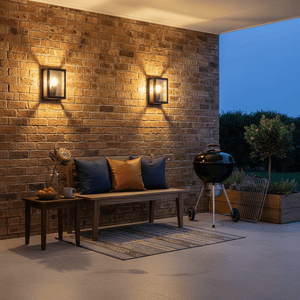 Two galvanized wall lights illuminate a brick patio with a bench and grill.