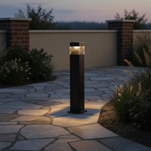 LED bollard light illuminating a stone pathway, surrounded by grass and shrubs at dusk.