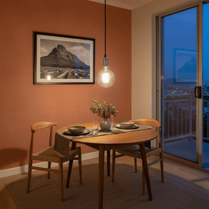 Chrome pendant light illuminating a dining table with two chairs, set against a warm-toned wall and framed artwork.