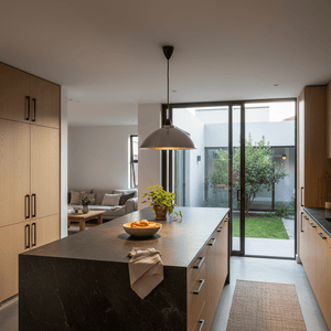 Aluminium pendant light hanging over a kitchen island with a bowl of fruit and a potted plant.