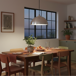 Lit aluminium dome pendant hanging above a wooden dining table with chairs, plants, fruit, and a window.