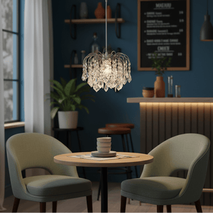 Polished chrome pendant light with clear acrylic crystals hanging above a small dining table with green chairs.