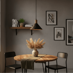 Black iron pendant light hanging above a wooden dining table with a vase of pampas grass.