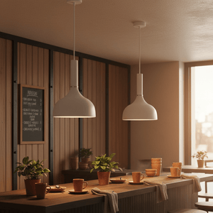 Two white metal pendant lights hang above a wooden kitchen island, surrounded by plants and tableware.