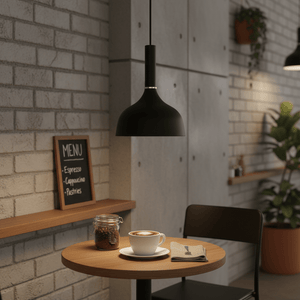 Black metal pendant light illuminating a coffee cup on a wooden table in a cozy cafe setting.