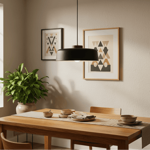 Black metal pendant light hanging above a wooden dining table set with dishes and a plant nearby.