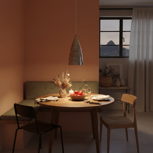 Aluminium pendant light hanging over a round dining table set with fruits and candles in a cozy indoor setting.