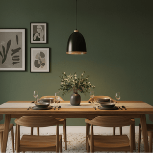 Black iron pendant light hanging over a wooden dining table set with plates and glasses, against a green wall.