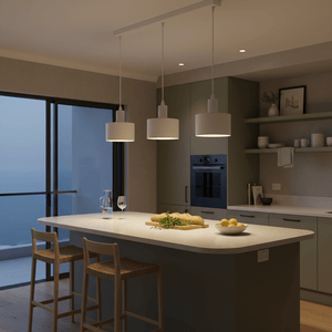 Three white metal pendant lights hang over a kitchen island, illuminating a countertop with food and drinks.