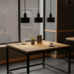 Three black metal pendant lights hang above a wooden table set with cups and a small plant.