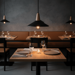 Dining setting with black metal and wood pendant lights illuminating wooden tables, set with plates, glasses, and candles.