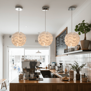 Three white wavy pendant lights hanging above a wooden counter in a café setting.