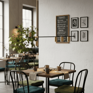 Black and gold metal pendant light above a dining table set with mugs and cutlery in a café setting.