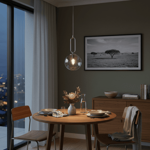 Satin chrome pendant light with clear glass shade hanging above a wooden dining table set for two.