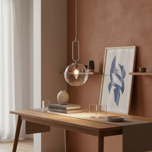Satin chrome pendant light with clear glass shade hanging over a wooden table with decor items.