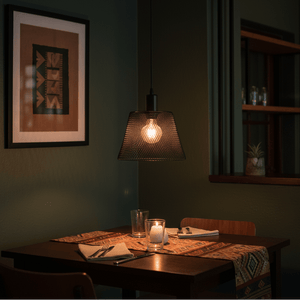 Black steel-mesh pendant light hanging above a dining table set with a candle and glassware.