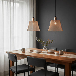 Two rose gold mesh pendant lights hanging over a wooden dining table set with dishes and a vase.