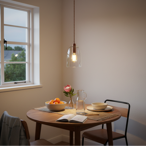 Bronze pendant with red cord and clear glass shade hanging above a styled wooden dining table beside a window.
