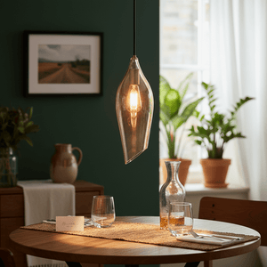 Satin brass pendant light with cognac glass shade hanging above a dining table set with glasses and a carafe.