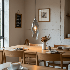 Satin nickel pendant light with smoke glass shade hanging over a wooden dining table set with plates and a vase.