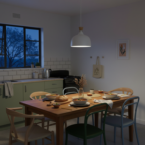 A white metal and wood pendant light hangs above a wooden dining table set with bowls and a loaf of bread.