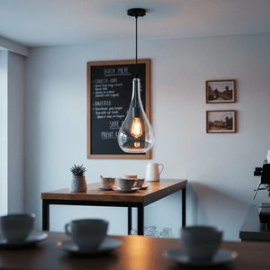Stylish black metal pendant light with clear glass shade hanging above a wooden table set with cups.