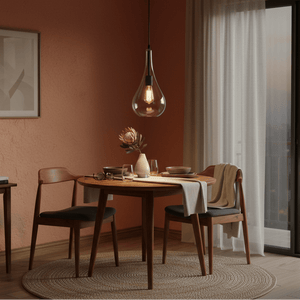 Modern black metal pendant light with clear glass shade hanging above a wooden dining table set.