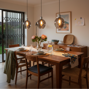 Stylish dining area featuring three polished chrome pendant lights with smoke glass shades above a wooden table set for a