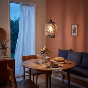 A cozy dining setup featuring a Metal and Rattan Pendant Light above a wooden table with a vase and bread.