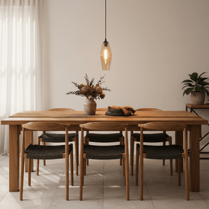 Amber glass pendant light hanging above a wooden dining table set with plates and a vase of flowers.