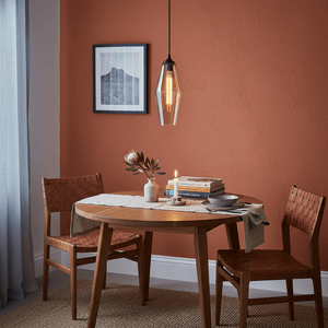 Amber glass pendant light hanging over a round wooden dining table with two chairs, books, and a candle.
